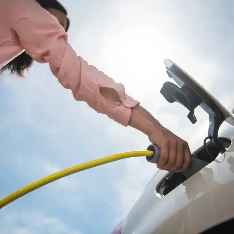 Person charging electric vehicle with cable